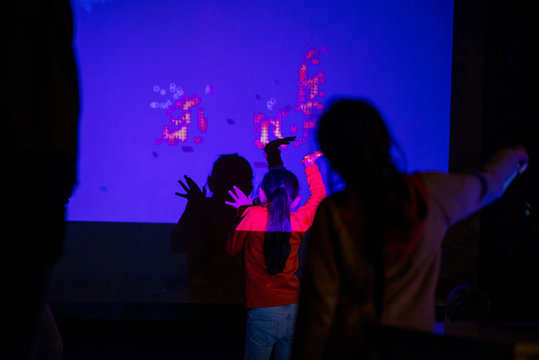 Abstract, Blurry New Technology Background. Little Girl Is Playing With Interactive Visual Installation Projected On Wall  