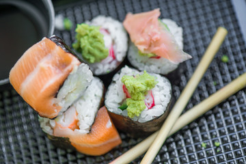 Fresh and delicious maki and nigiri sushi rolls with tiger shrimps, salmon, philadelphia cheese and wasabi served with soy sauce and ginger slices on black take away plate. Japanese food in restaurant