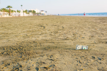 Fototapeta na wymiar Banknote of value of one dollar in the the sand on the beach. Concept of cheap travel and vacation. Promotion and discount