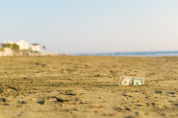 Banknote of value of one dollar in the the sand on the beach. Concept of cheap travel and vacation. Promotion and discount