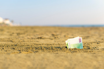 Fototapeta na wymiar Banknote of value of one hundred euro in the the sand on the beach. Concept of cheap travel and vacation. Promotion and discount