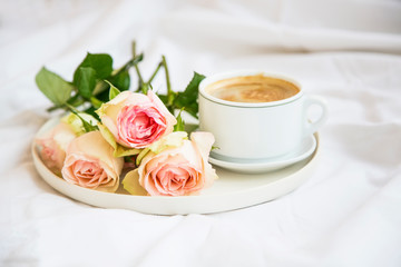 Morning coffee cup with roses bouquet in a tray in bed, romantic bed breakfast or coffee with flowers bouquet
