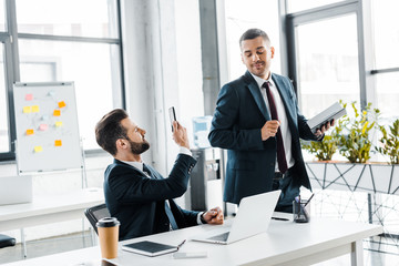 selective focus of handsome businessman taking photo of cheerful coworker