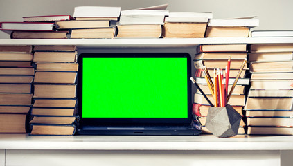 Green screen laptop, stack of books, notebooks and pencils on white table, education office concept background.