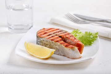Grilled red salmon steak served with lemon and lettuce on white plate. Sockeye salmon, kokanee salmon or Oncorhynchus nerka.