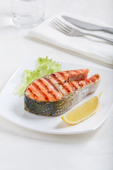 Grilled red salmon steak served with lemon and lettuce on white plate. Sockeye salmon, kokanee salmon or Oncorhynchus nerka.