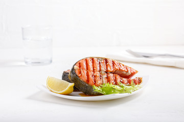 Grilled red salmon steak served with lemon and lettuce on white plate. Sockeye salmon, kokanee salmon or Oncorhynchus nerka.