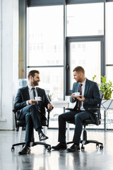 cheerful businessmen talking while holding cups with drinks