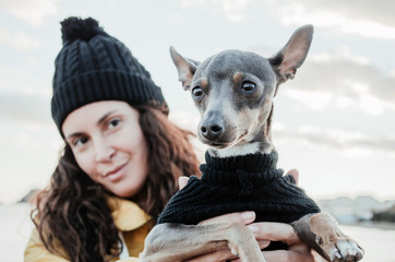 Young and brunette woman with her little dog on the beach with yellow raincoat and hat.