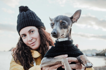Young and brunette woman with her little dog on the beach with yellow raincoat and hat.