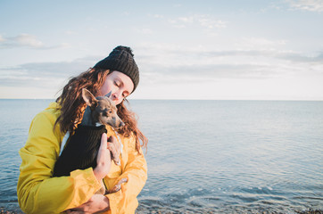 Young and brunette woman with her little dog on the beach with raincoat and hat.