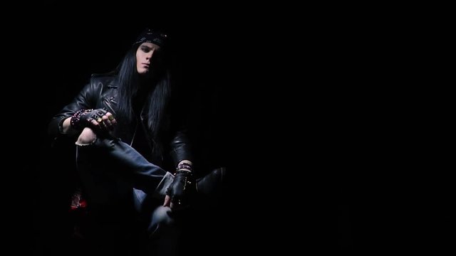 Tough looking rocker with bandana and ripped jeans crosses his legs, slight slow motion