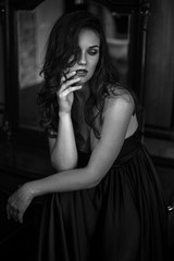Portrait of young woman in elegant silk black dress posing in a dark interior, fashion beauty photo