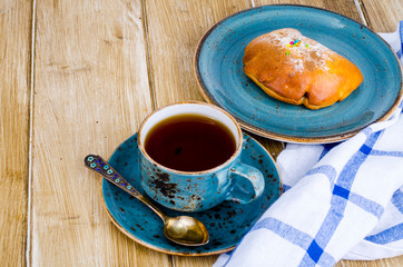 Fresh bun and cup of tea on wooden table for breakfast
