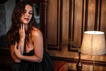 Plakat Portrait of young woman in elegant silk black dress posing in a dark interior, fashion beauty photo