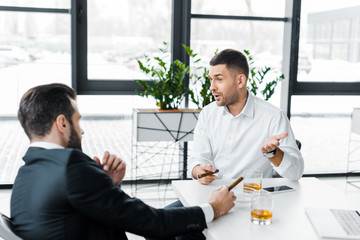 businessmen in formal wear smoking cuban cigars in modern office