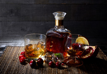 cognac with a lemon, pomegranate and cherry on a wooden background with fire.Fiery drinks on...
