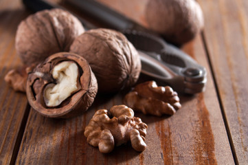 Walnuts peeled and inshell. In the background is a nutcracker. Brown wooden table.