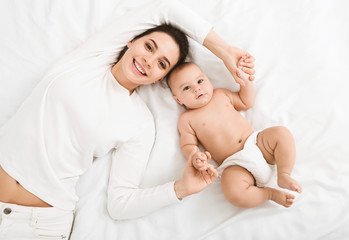 Happy mother and baby lying on bed top view