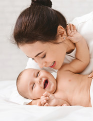 Mother tickling her baby playing in bed at home