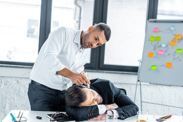 focused man drawing with marker on face of sleeping coworker in modern office