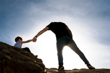 young father giving helping hand to his son climbing the rocks as a metaphor of life challenges