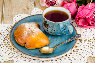 Fresh bun and cup of tea on wooden table for breakfast