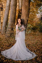 Bride in boho style surrounded by autumn foliage on sunny day