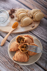 Traditional curry puffs stuffed chicken with raw curry puffs on wooden table as background