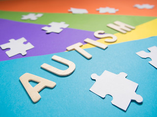 World Autism Awareness Day concept. Autism wood word with white jigsaw puzzle on different geometric colors background. Creative idea. Selective focus. Close up.