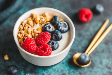 Vegetarian breakfast, a bowl with organic granola, fresh raspberries and blueberries and coconut yoghurt.