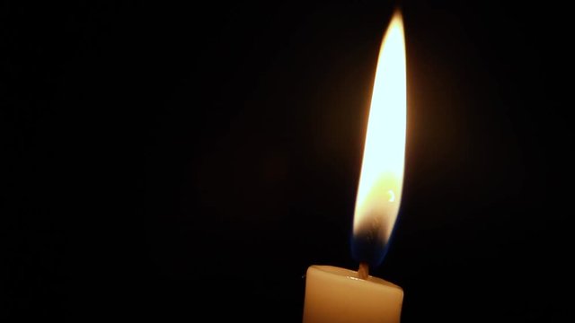Close up view of a candle against a black background almost will with a soft breeze coming in making it move and settle