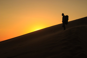 Fototapeta na wymiar A white male traveler in sportswear with a backpack on his back is standing on the orange sand of a dune in Soususfleu National Park, Namibia at sunset
