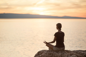Young woman practicing yoga near the sea at sunset. Harmony, meditation  and travel concept. Healthy lifestyle