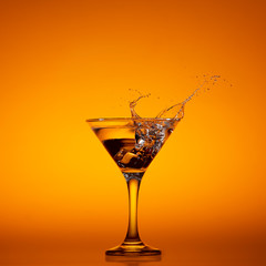 Cocktail che schizza da bicchiere martini su fondo arancio.