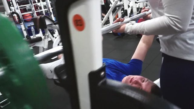 Female trainer help newbie to perform barbell bench bar press exercise in gym. Overhead angle shot