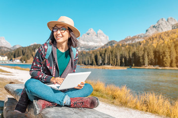 Happy Asian woman working on laptop on mountain lake background in autumn. The concept of remote...