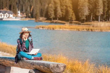 Foto op Canvas Happy Asian woman working on laptop on mountain lake background in autumn. The concept of remote work and freelancer © EdNurg
