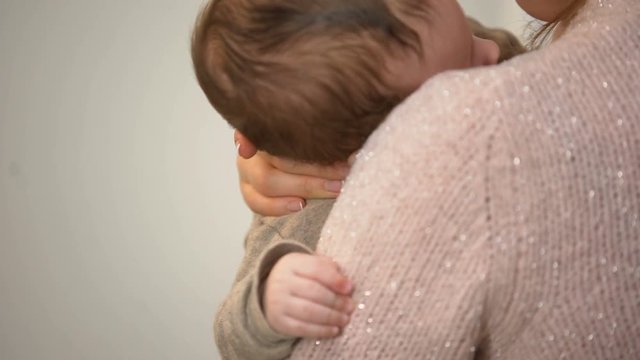 Young mother cuddling adorable infant in arms, tiny hand closeup, baby care