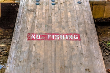 No Fishing sign on wooden deck over murky water