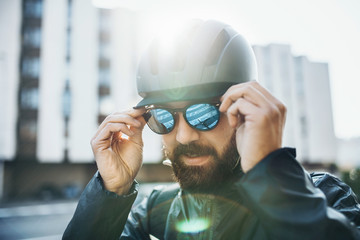Male bicycle courier with helmet putting on sunglasses in city.