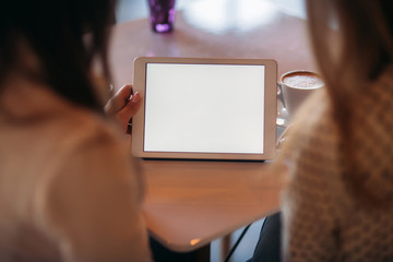 Two girls use a tablet while sitting in a cafe and drinking coffee. Business woman