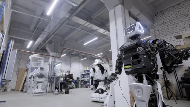 Factory for the production of robots, modern robotic developments. The disassembled robot waves his hands in greeting and dances in the workshop. Engineers walk in the background