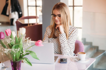 Business woman with laptop and phone in cafe. Happy young girl working