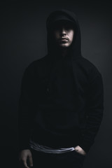 Obraz na płótnie Canvas young cool rapper with black hoodie and cap standing in front of grey background