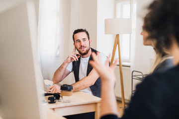 Fototapeta premium A portrait of young businessman in a modern office, talking to unrecognizable colleagues.