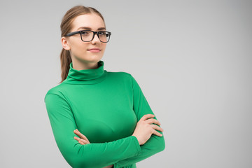 Serious  young woman  in glasses and in casual clothes posing in the studio with crossing hands. Horizontal image - obrazy, fototapety, plakaty