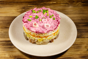 Traditional russian salad "Herring under a fur coat" (shuba) on wooden table. Layered salad with herring, beets, carrots, onions, potatoes and eggs
