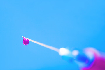 Macro of hypodermic needle. drop of pink drug