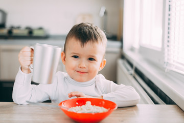 A child in the kitchen eating their own oatmeal with a red plate